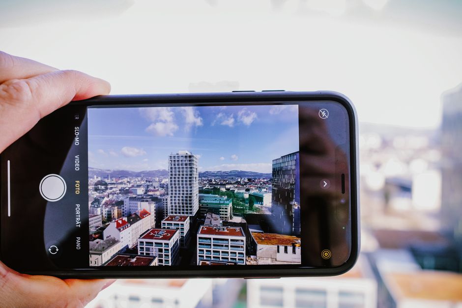 Detailní záběr ruky držící smartphone, na displeji se zobrazuje fotografie s vylepšenými barvami a expozicí díky AI.