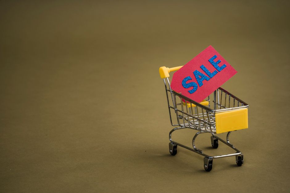 Nákupní košík plný produktů s cenovkami a zvětšovací sklo, zdůrazňující důležitost porovnávání cen a detailů produktu.