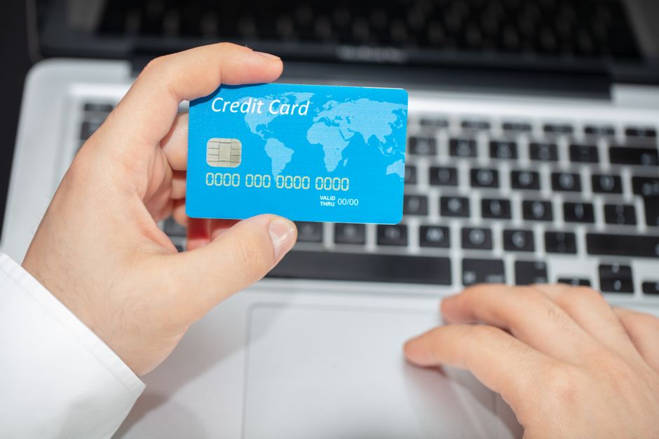Ruce drží platební kartu u mobilního telefonu, na obrazovce je ikona zabezpečené platby, což ilustruje bezpečné online nákupy a platby.