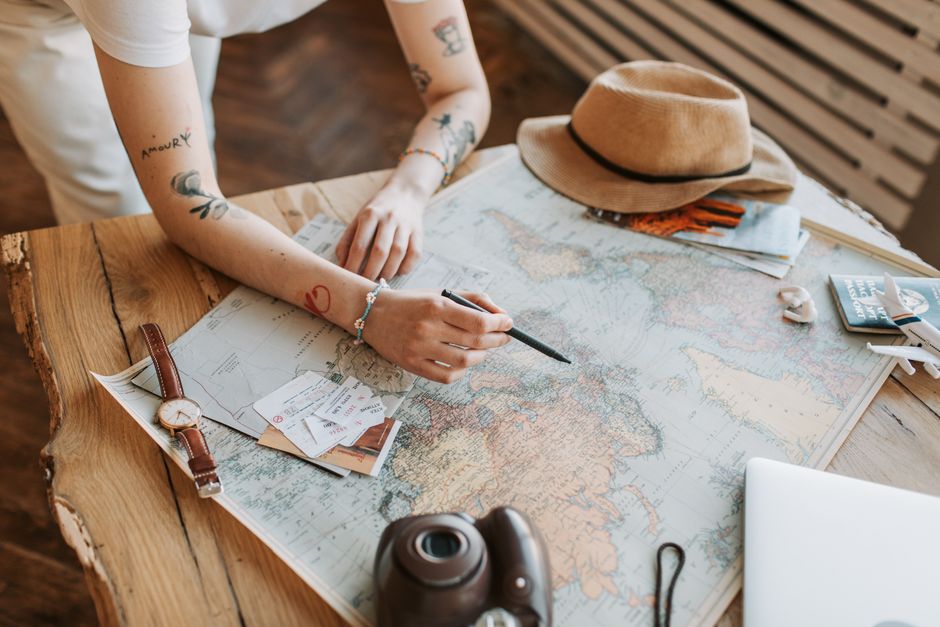 Primo piano di mani che consultano un laptop aperto su una mappa del mondo, con passaporto e taccuino accanto, simbolo di pianificazione viaggio.