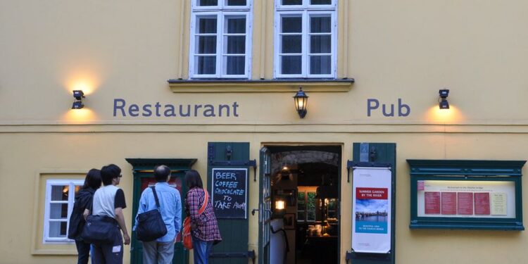 Menù di un ristorante turistico con foto e traduzioni in diverse lingue, in una via affollata.