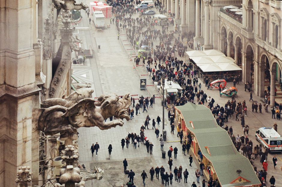 Gruppo di turisti in una piazza europea affollata, con persone che cercano di vendere braccialetti.