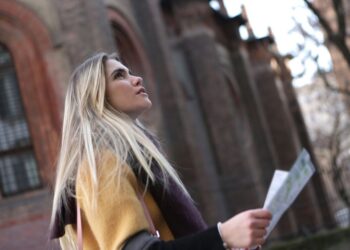 Donna con zaino che consulta una mappa in una piazza europea, con edifici storici sullo sfondo.