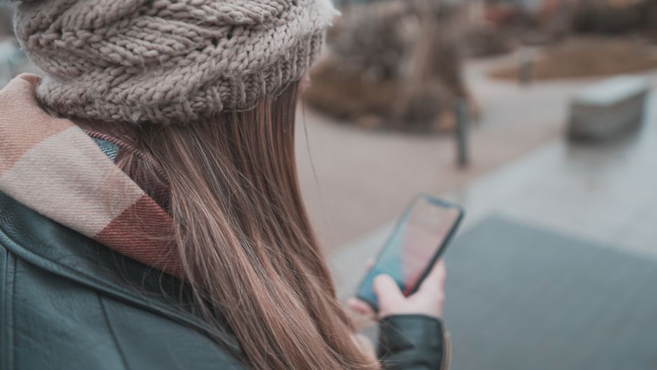 Žena si prohlíží předpověď počasí na svém telefonu, aby naplánovala sezónní outfity.
