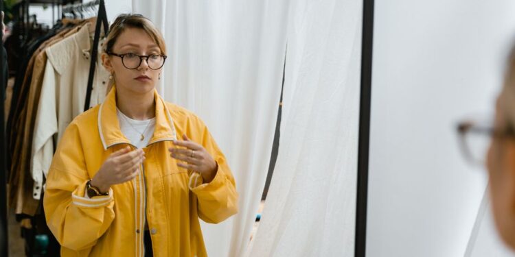 Žena zkoušející béžový trenčkot před zrcadlem